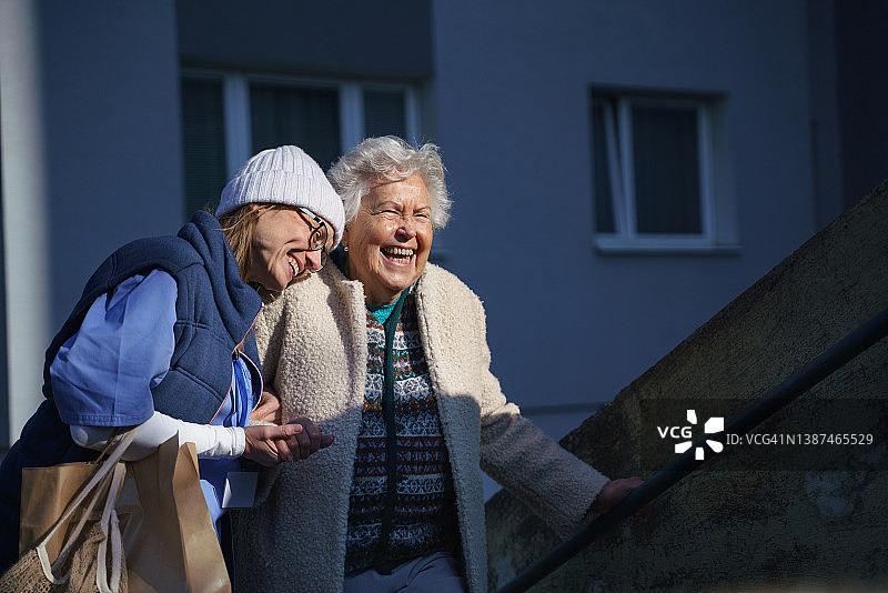 年长的女人和护理人员在镇上散步，欢笑着图片素材