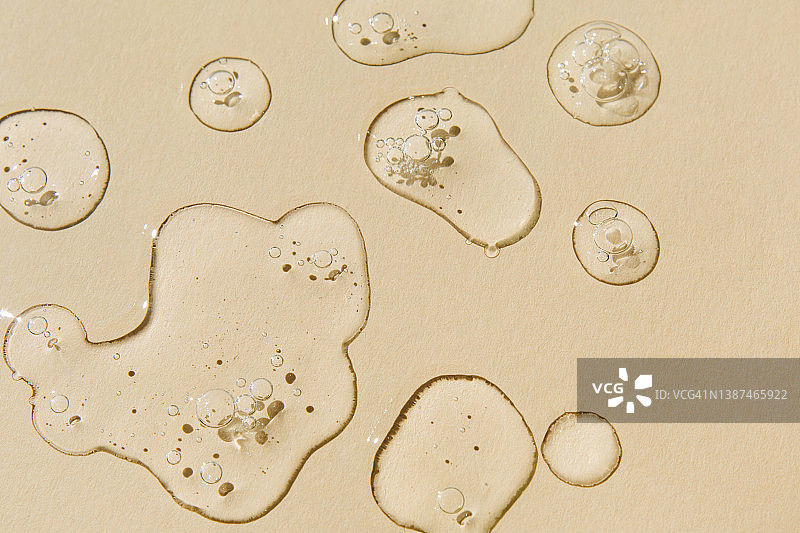 米色背景上的透明精华液滴，透明质酸凝胶，展平俯视图片素材