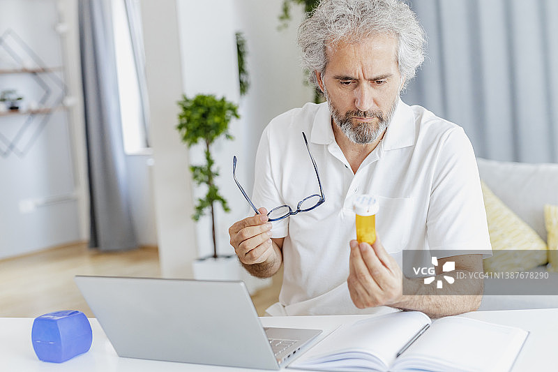 年长的男人在网上搜索关于药物的信息，手里拿着一瓶药图片素材