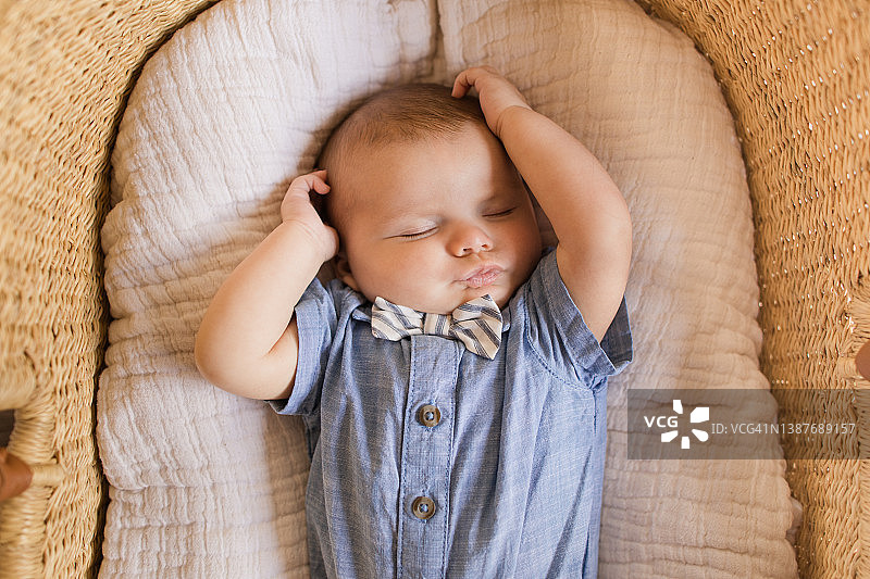 一名12周大的男婴患有多指症，舒适地躺在海草摩西篮里的奶油色棉毯上图片素材