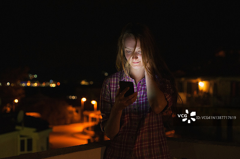 夜晚户外发短信的红发年轻女子图片素材