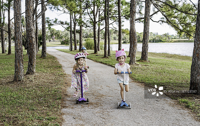 一群可爱的孩子，朋友们戴着安全头盔在户外一起使用滑板车玩耍图片素材
