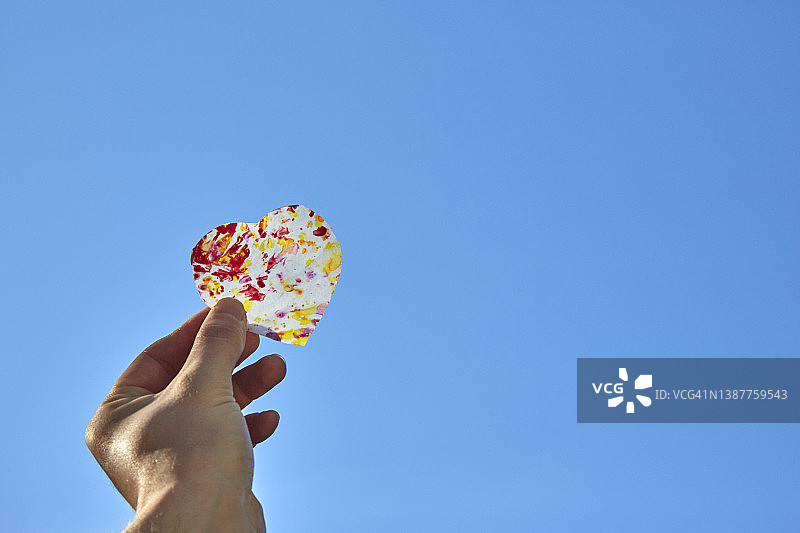 手持透明心形剪纸，背景为蓝天图片素材