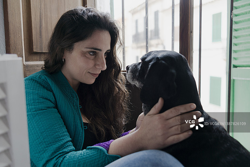 坐在房间地板上看着她的狗眼睛的年轻女人图片素材