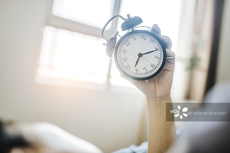 年轻女子在床上睡觉，手拿闹钟图片素材