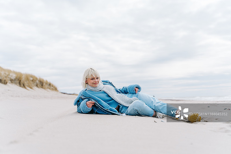 穿着牛仔服的年轻潮人短发女子躺在海边的沙滩上图片素材