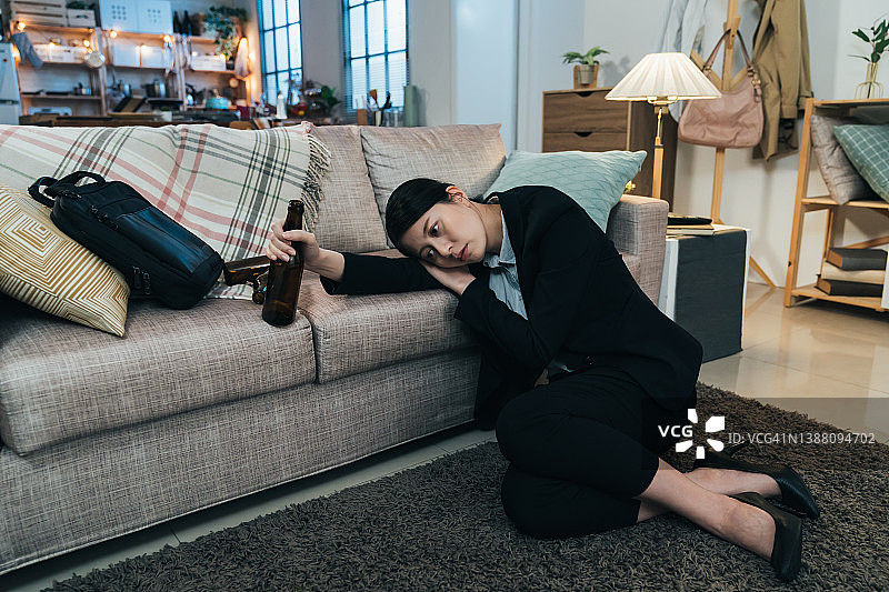中国台湾千禧一代女性身穿西装，头靠沙发，陷入黑色抑郁，手持酒瓶不愿面对工作问题图片素材