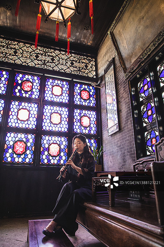 年长的亚洲妇女在中国传统房屋里吹尺八图片素材