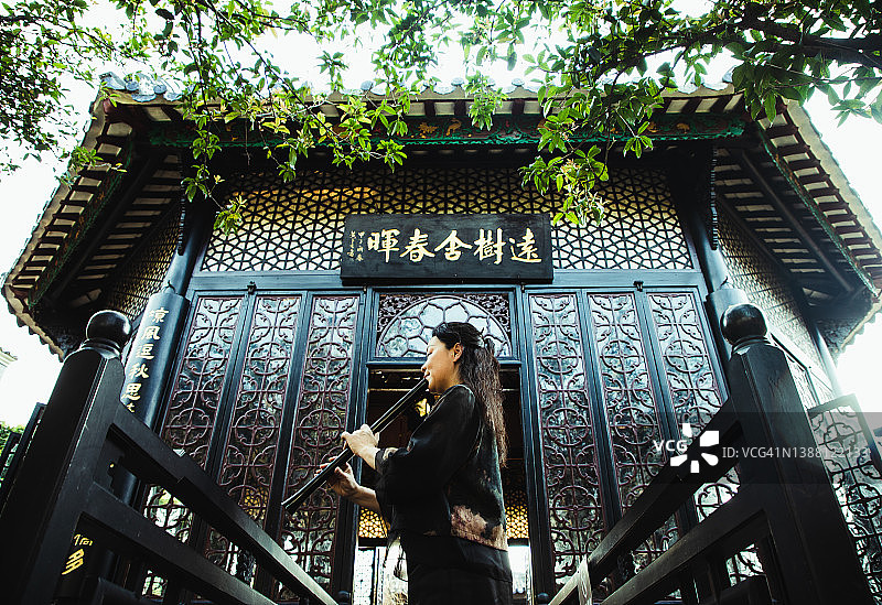 年长的亚洲女性在中国传统花园里练习尺八图片素材