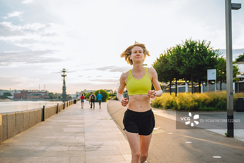 年轻运动女性在阳光明媚的夏日早晨沿着城市堤岸慢跑图片素材