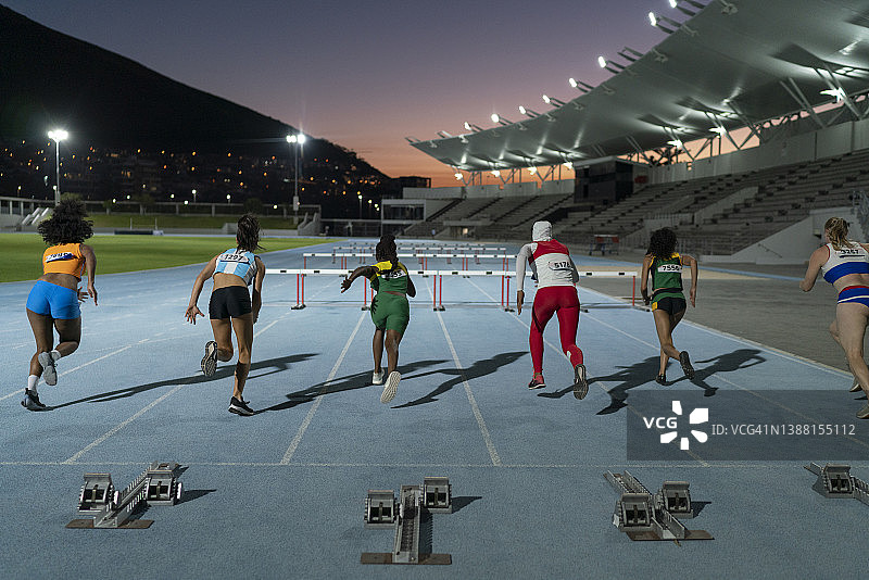 田径女运动员在夜间赛道上跨越栏架图片素材