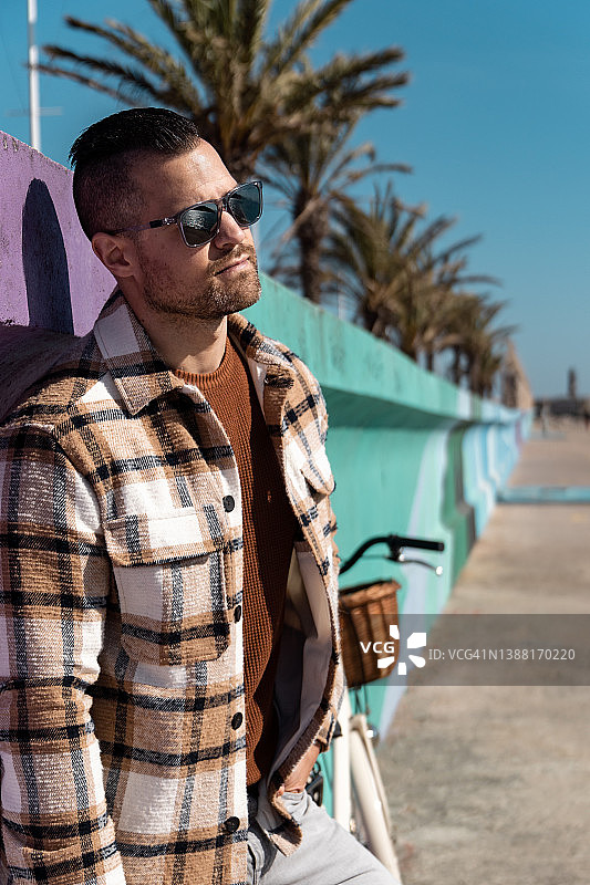 戴墨镜的现代年轻男子骑自行车在海边的人像照片图片素材