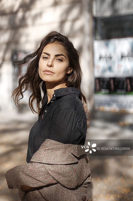 穿着棕色外套和黑色衬衫，好奇地看着镜头的棕色眼睛可爱女孩图片素材