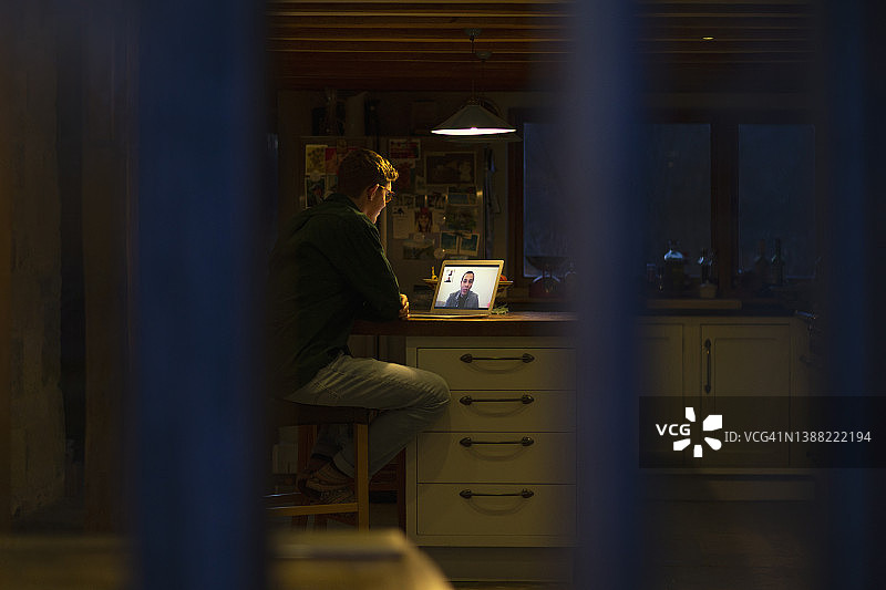 男人在黑暗的厨房里用笔记本电脑进行深夜视频会议图片素材