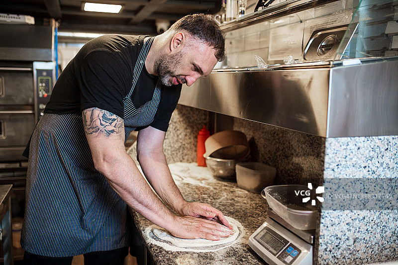 男人在餐厅厨房的柜台上揉搓披萨面团图片素材