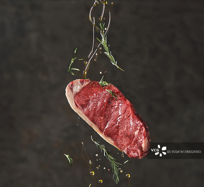 飞舞的生牛排与倾倒的油，以及洒落的香草和香料图片素材