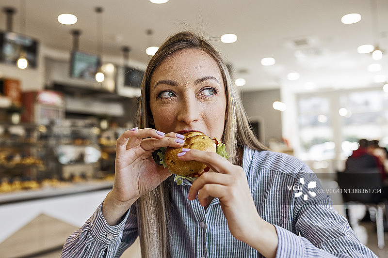 年轻金发女子正在吃美味的小三明治图片素材