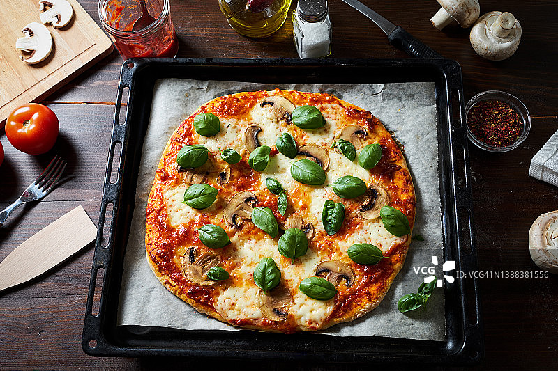 在家烹饪意式蔬菜蘑菇披萨，可在披萨店、面包店或咖啡馆食用。热披萨配罗勒叶和奶酪，放在烤盘上即可食用。美食概念：自制披萨步骤一图片素材
