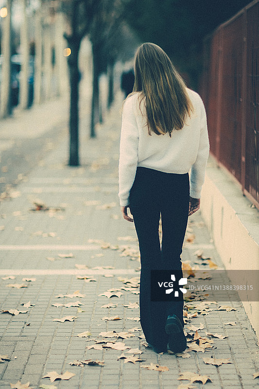 年轻女子在秋季的街道上行走的背影图片素材