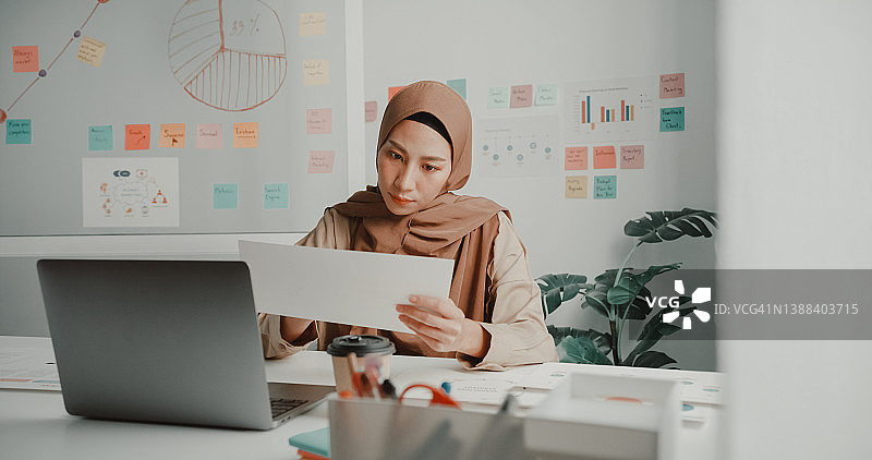 年轻的亚洲穆斯林女商人戴着头巾在办公室的桌子上用笔记本电脑工作图片素材