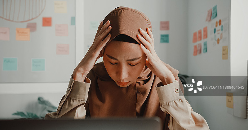 戴着头巾、在办公室办公桌前使用笔记本电脑的沮丧年轻亚洲穆斯林女商人图片素材