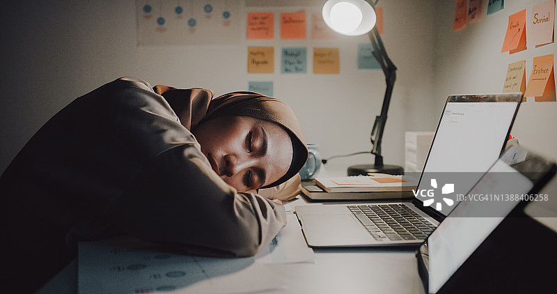 疲惫的年轻亚洲穆斯林女商人戴着头巾在办公室的办公桌旁努力工作图片素材