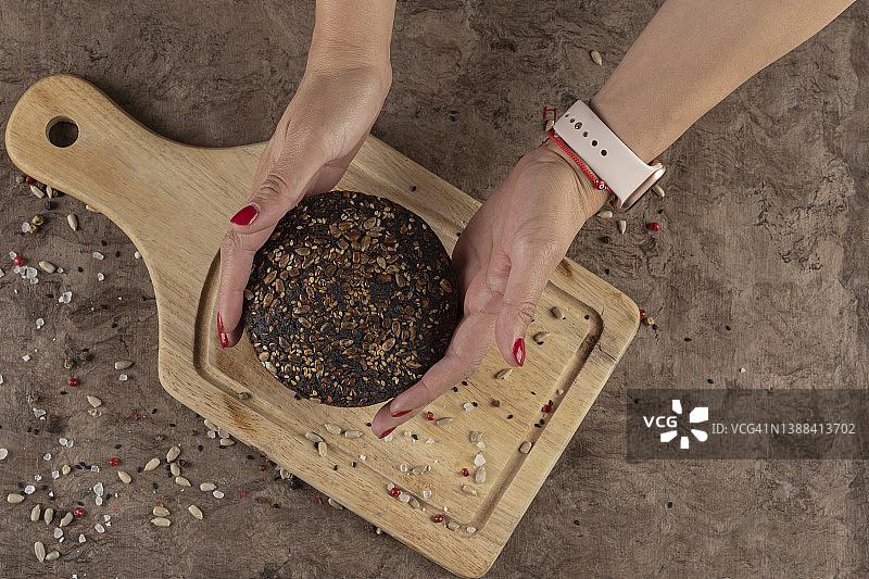 女人将黑麦面包放在砧板上，桌上撒着种子：自制糕点或面包店的概念图片素材