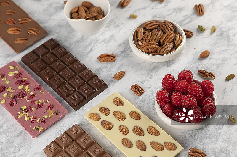 灰色桌面上带有杏仁、核桃和红色水果的各种口味巧克力，留有文字空间图片素材