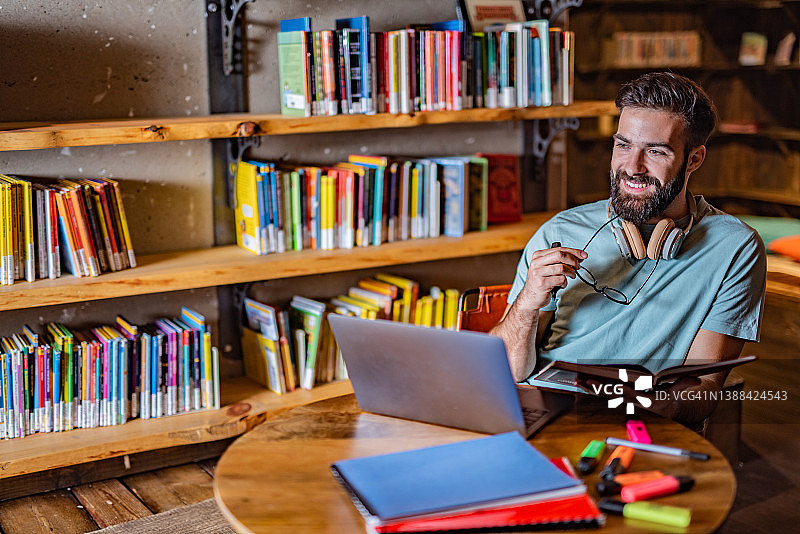 年轻教授在办公室使用笔记本电脑并拿着一本书图片素材