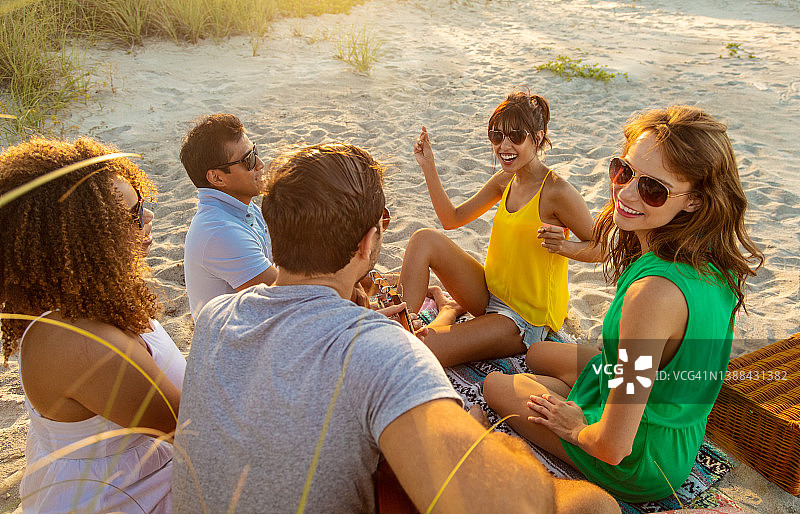 多种族朋友在日落时分在海滩上放松图片素材