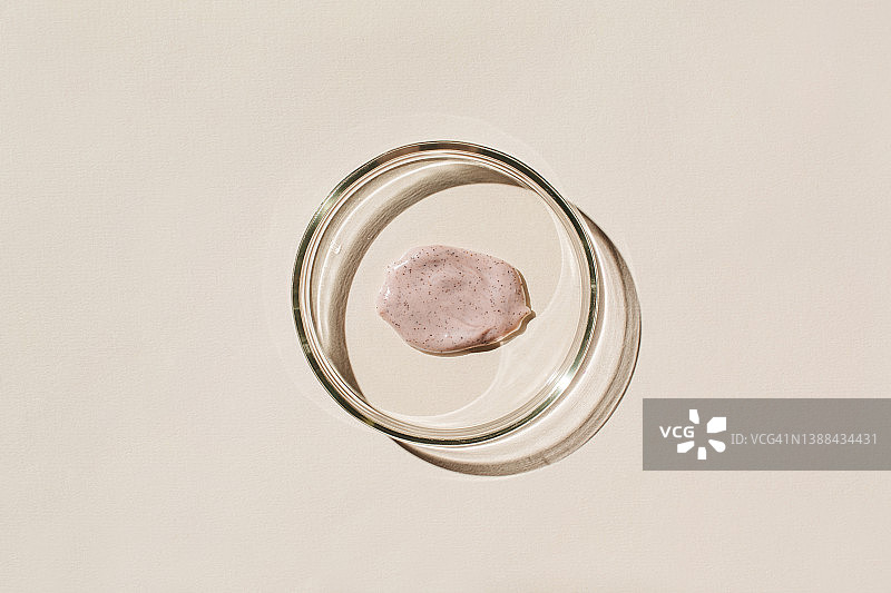 培养皿，含去角质颗粒的涂抹磨砂膏，米色背景。化妆品实验室研究概念。皮肤病学科学。天然药物，化妆品研究，有机美容产品。俯视图，平铺。图片素材