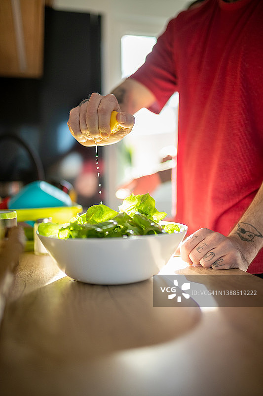 手握柠檬片，将汁挤到厨房台面上碗里的生菜上图片素材