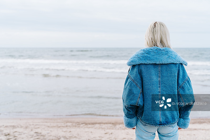穿着牛仔夹克的金发短发年轻女子站在海边眺望远方图片素材