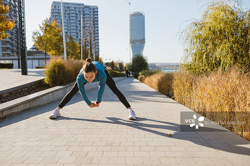 站在走道上，双腿分开向前弯曲，为慢跑热身的年轻女人图片素材