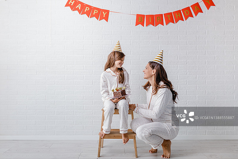 女孩拿着生日蛋糕坐在凳子上的肖像，母亲在她旁边图片素材