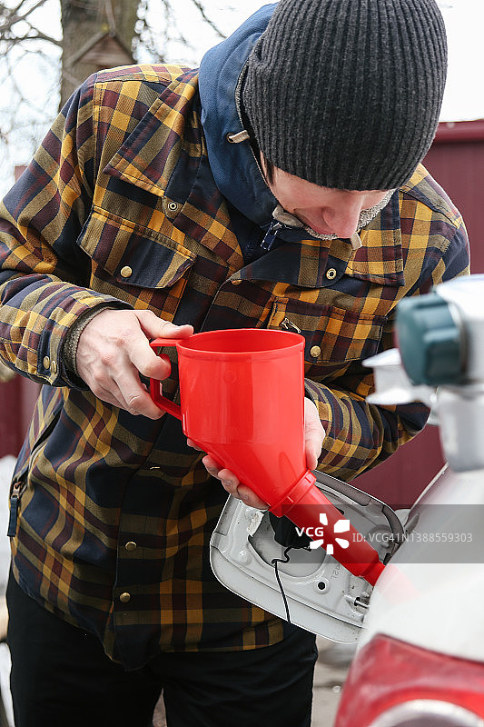 年轻男子用红色漏斗和罐子给汽车加油图片素材