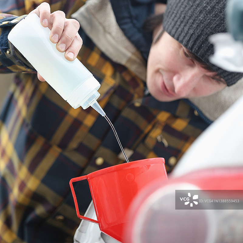 青年男子用红色漏斗和小瓶汽油给汽车加油图片素材