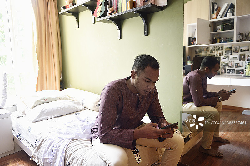 在卧室里使用手机的新加坡印度裔男子图片素材