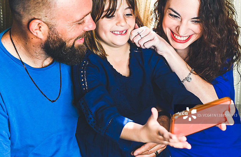 一家人一起用手机自拍或录像，母亲、父亲和女儿亲密有爱的家庭时刻图片素材