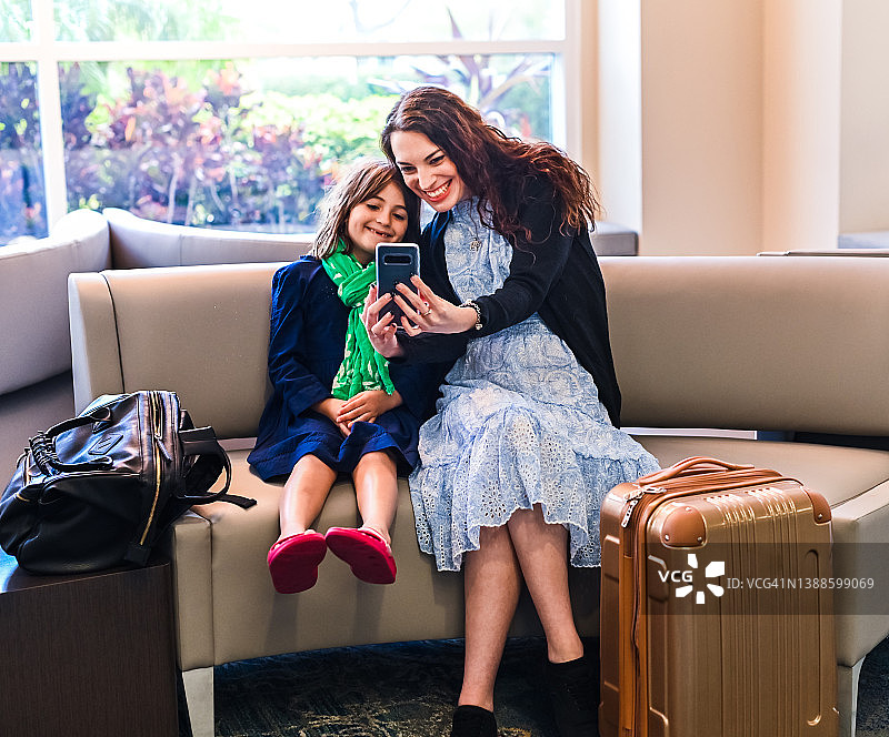 母女在家庭旅行中于酒店大堂或机场用手机合影，携带着行李图片素材