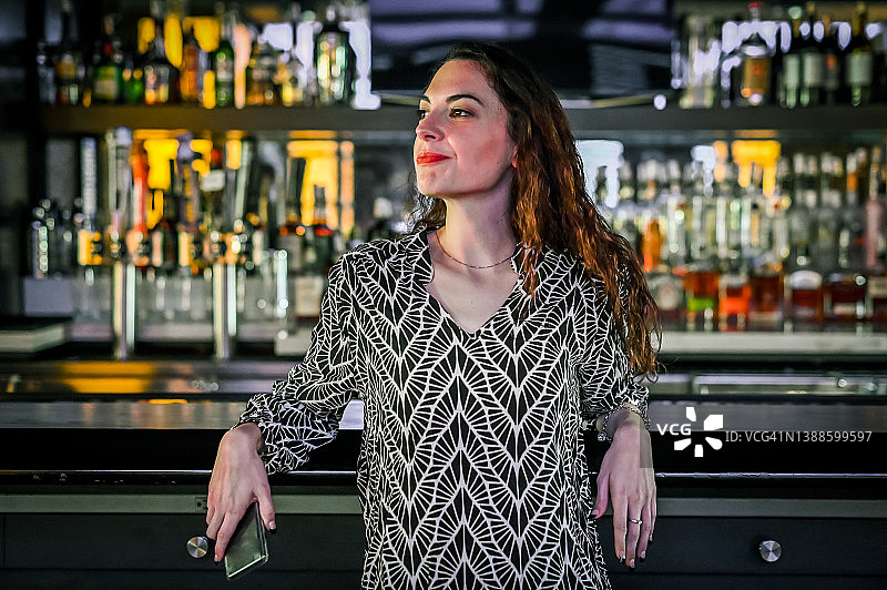 女人靠在酒吧上，身后是酒瓶，小企业主或酒保图片素材
