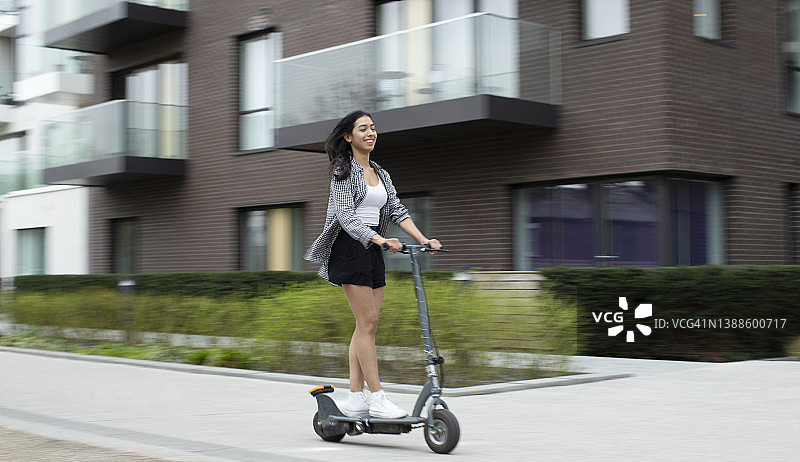 快乐的年轻女人在城市人行道上骑电动滑板车图片素材