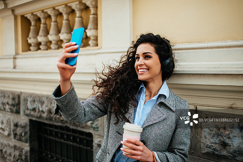 在城市背景中戴着耳机听音乐的年轻女孩肖像图片素材