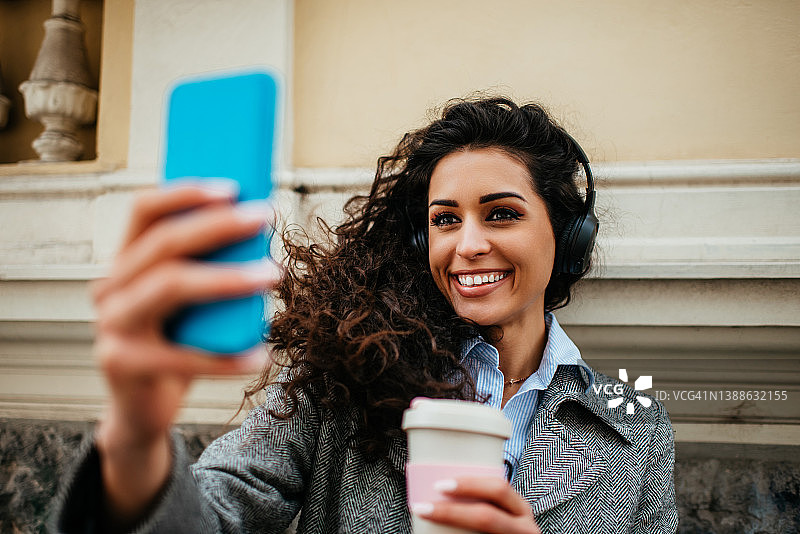 在城市背景中戴着耳机听音乐的年轻女孩肖像图片素材