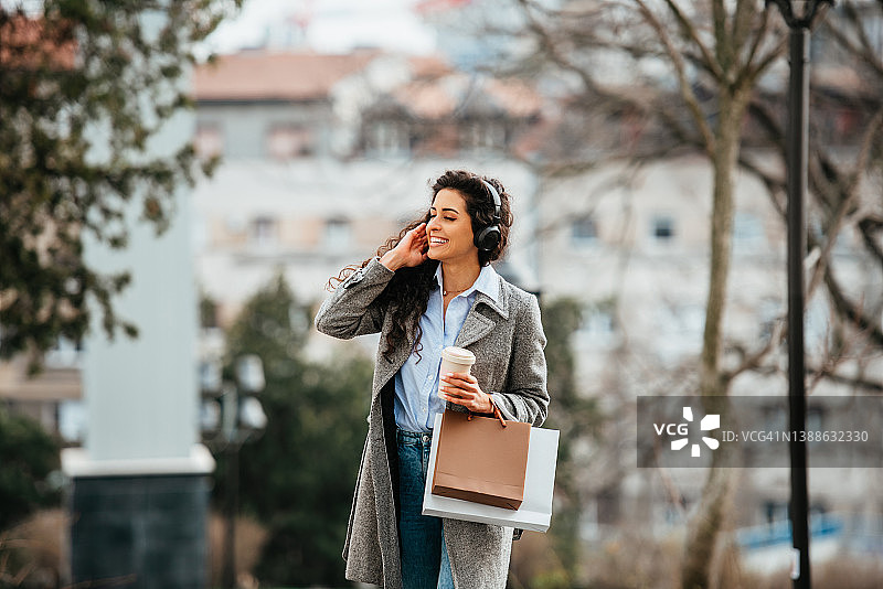 在城市背景中戴着耳机听音乐的年轻女孩肖像图片素材