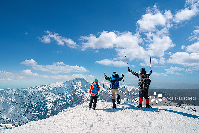 登山队成功登顶，在冬季高海拔雪山顶峰张开双臂，手持登山杖图片素材