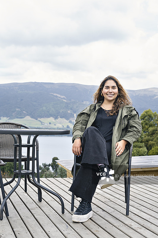 年轻女人坐在椅子上，面带微笑地看着镜头，休息并享受自由图片素材
