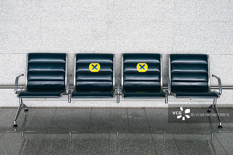 贴在机场椅子上的黄色标志新贴纸，与其他人相隔一个座位，保持距离，预防和防止COVID-19新冠病毒传播风险，隔离和疫情期间的空座位图片素材