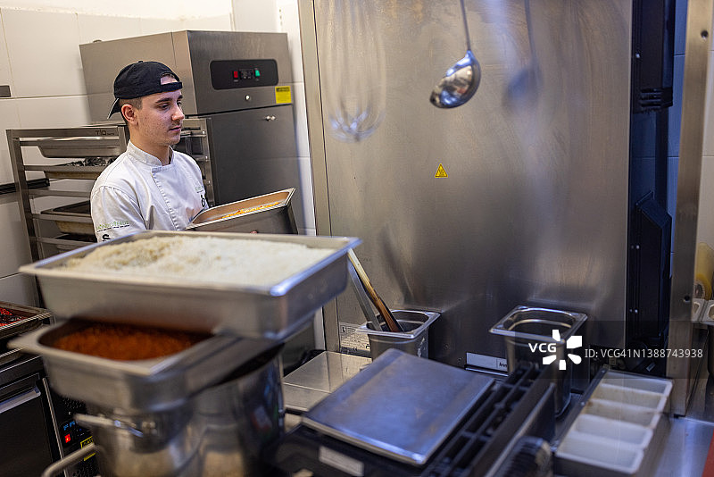 男厨师在快餐店厨房准备金属托盘和食材图片素材