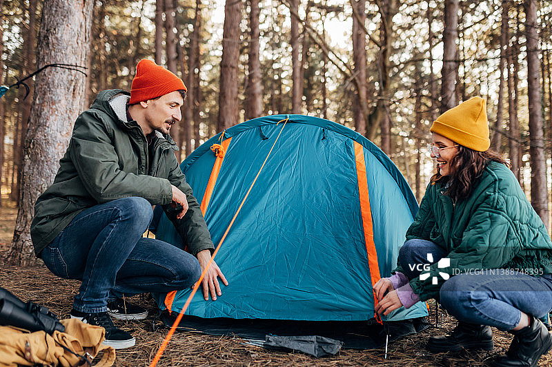 穿着暖和的衣服，露营者准备在野外过夜，搭建露营帐篷图片素材
